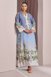 Woman wearing a long, light blue dress with floral patterns in a minimalistic setting.