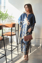 Woman in a blue floral dress standing in a modern indoor setting with plants and furniture.