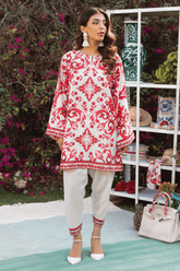 Woman wearing a red and white patterned dress with white pants, standing outdoors with floral background.