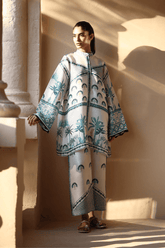 Woman wearing a patterned outfit standing in a sunlit room with columns.