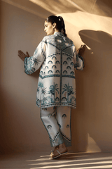 Woman wearing a patterned outfit standing against a plain wall.