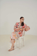 Woman in a colorful floral dress sitting on a white chair against a plain background