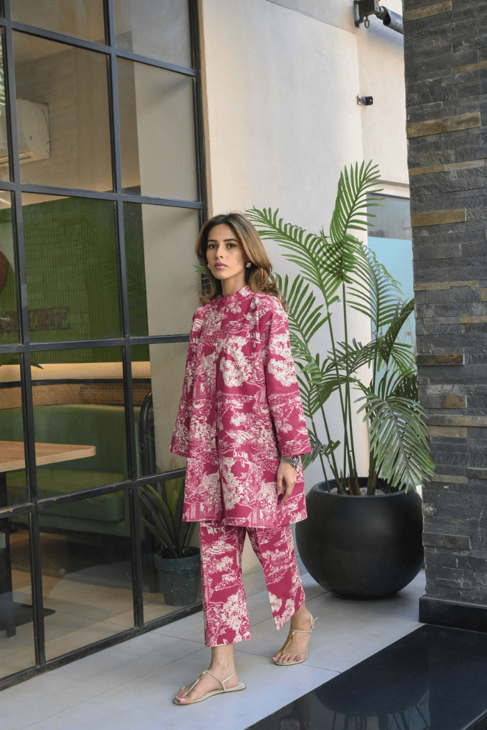 Woman in a pink floral outfit standing in an indoor setting with plants and modern decor.