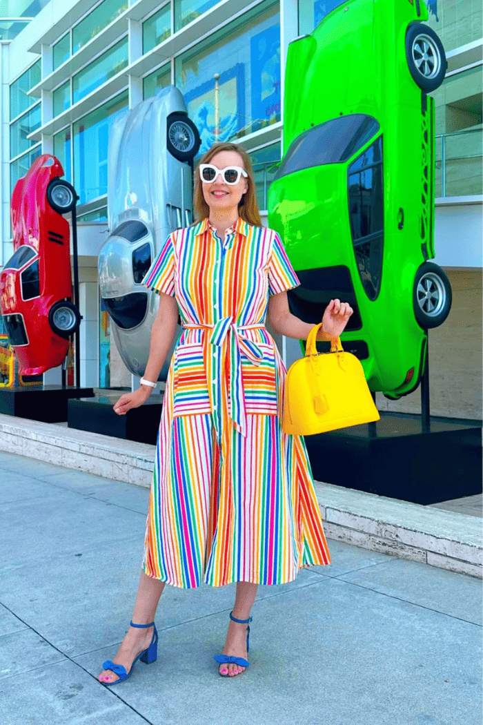 Woman in a colorful striped dress standing in front of large toy cars.