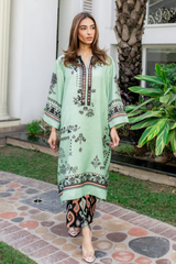 Woman wearing a light green embroidered dress with black patterns in an outdoor setting.