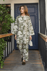 Woman in a floral outfit standing on a wooden deck with plants and a blue door in the background.