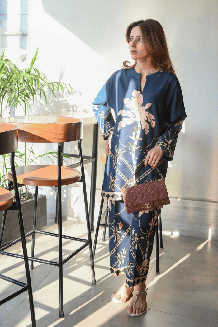 Woman in a blue floral dress standing in a modern indoor setting with plants and furniture.