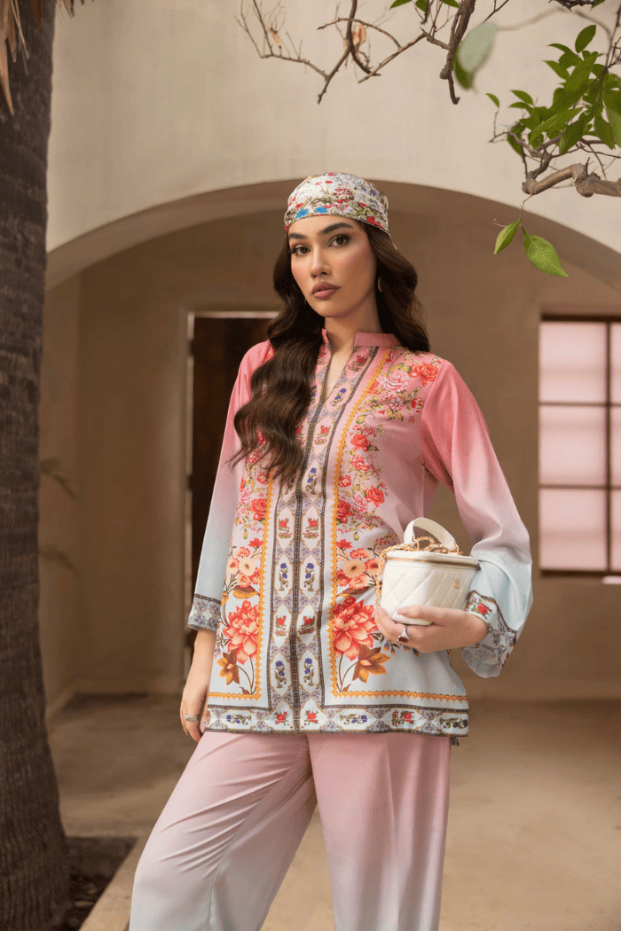 Woman in a floral blouse and pink pants holding a ceramic pot outdoors.