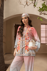 Woman in a floral blouse and pink pants holding a ceramic pot outdoors.