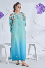 Woman wearing a light blue and green printed dress with floral decorations on a white background.