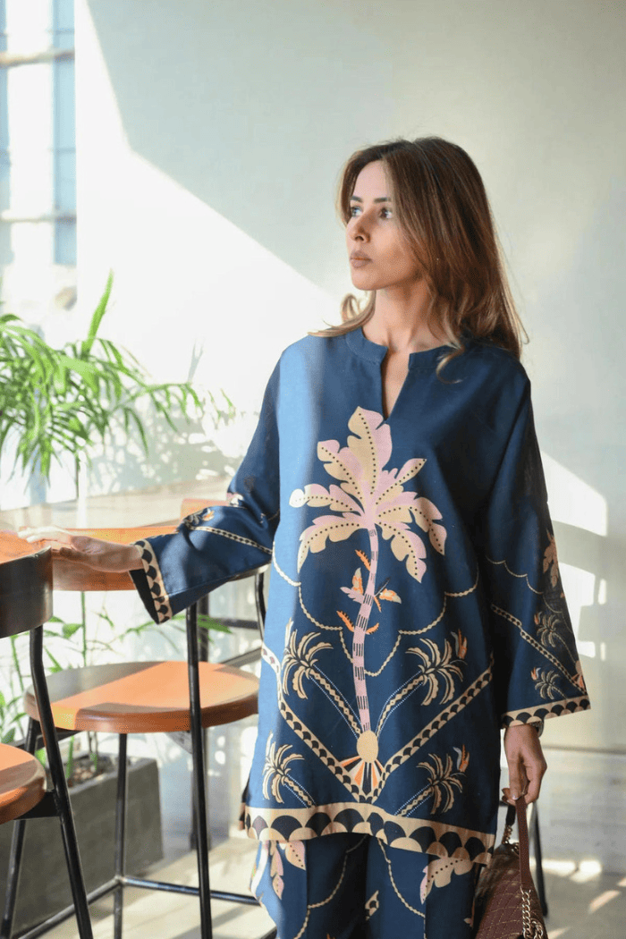 Woman wearing a blue floral dress in an indoor setting with plants and furniture.