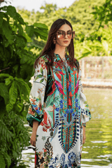 Woman in a colorful dress standing by a body of water with greenery in the background