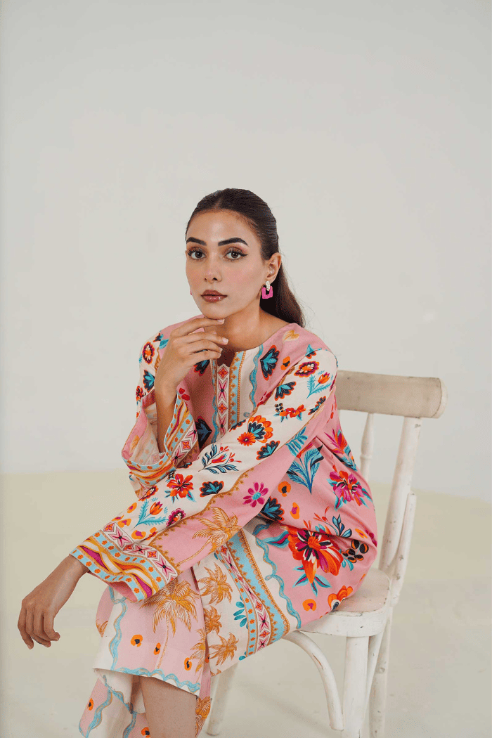 Woman sitting on a chair wearing a colorful floral dress against a white background