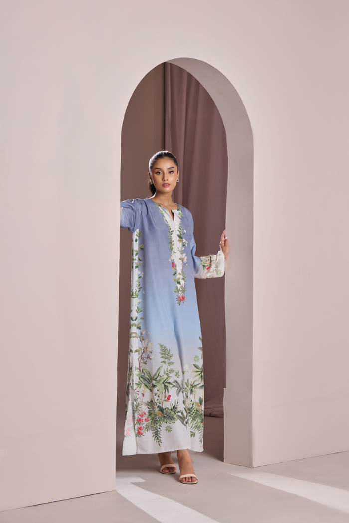 Woman in a light blue dress with floral patterns standing in an archway.