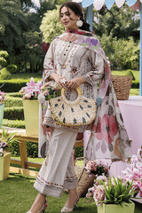 Woman in a floral outfit holding a woven bag in an outdoor setting with greenery and flowers.