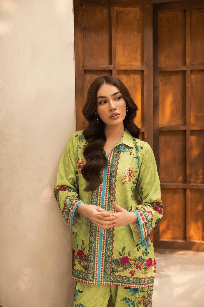 Woman wearing a green traditional outfit with floral patterns against a wooden door.