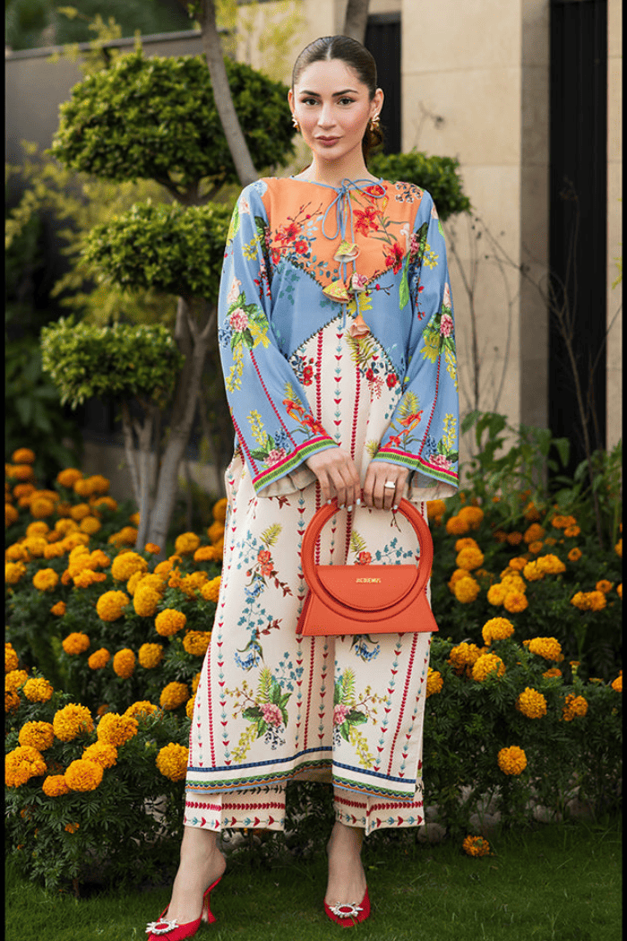 Woman in a colorful dress holding an orange handbag with flowers and greenery in the background