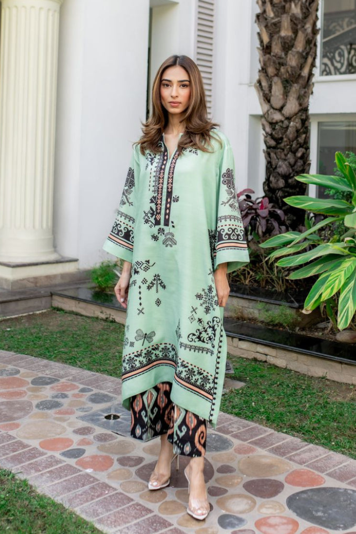 Woman wearing a light green dress with black floral patterns standing outdoors.