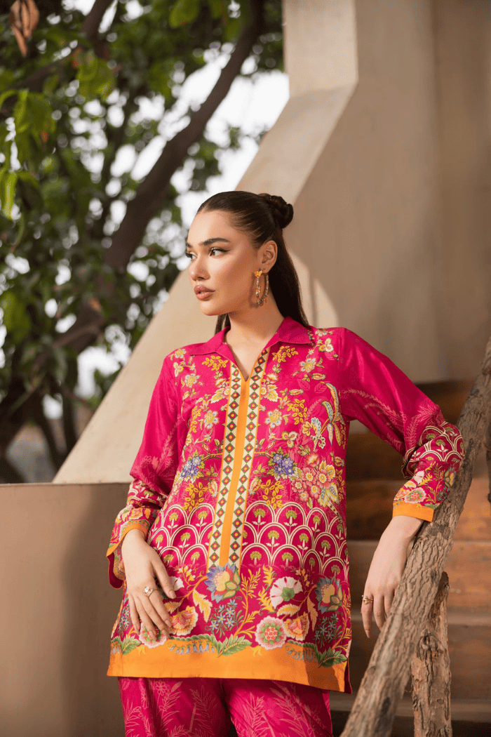 Woman wearing a vibrant pink traditional outfit with intricate patterns, standing outdoors.
