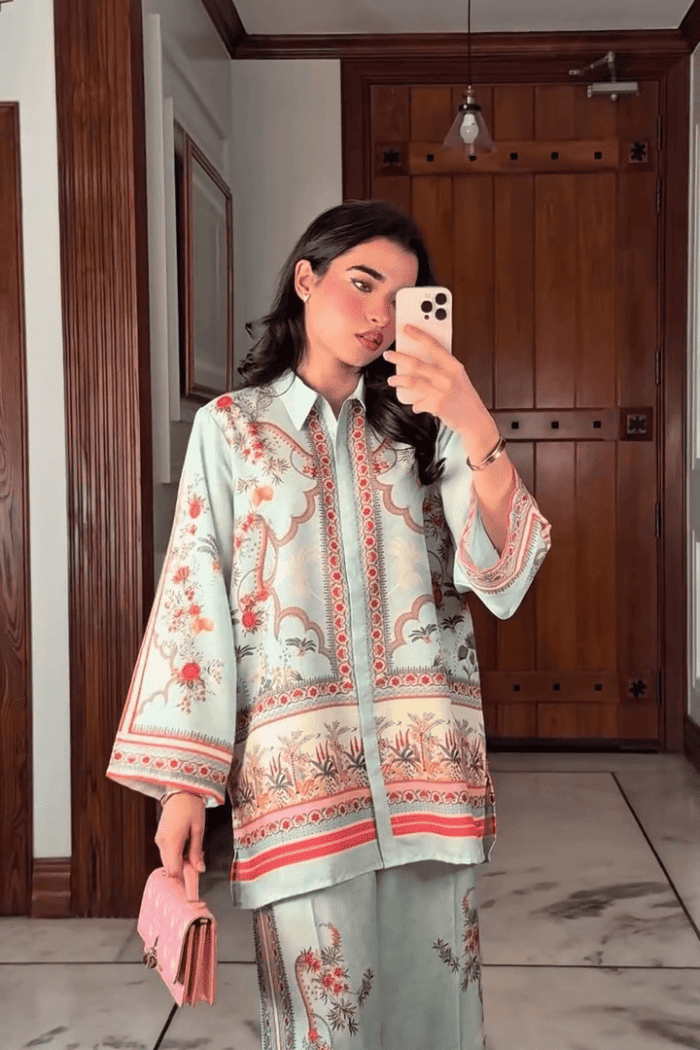 Woman taking a mirror selfie wearing a floral embroidered outfit in a room with wooden doors.