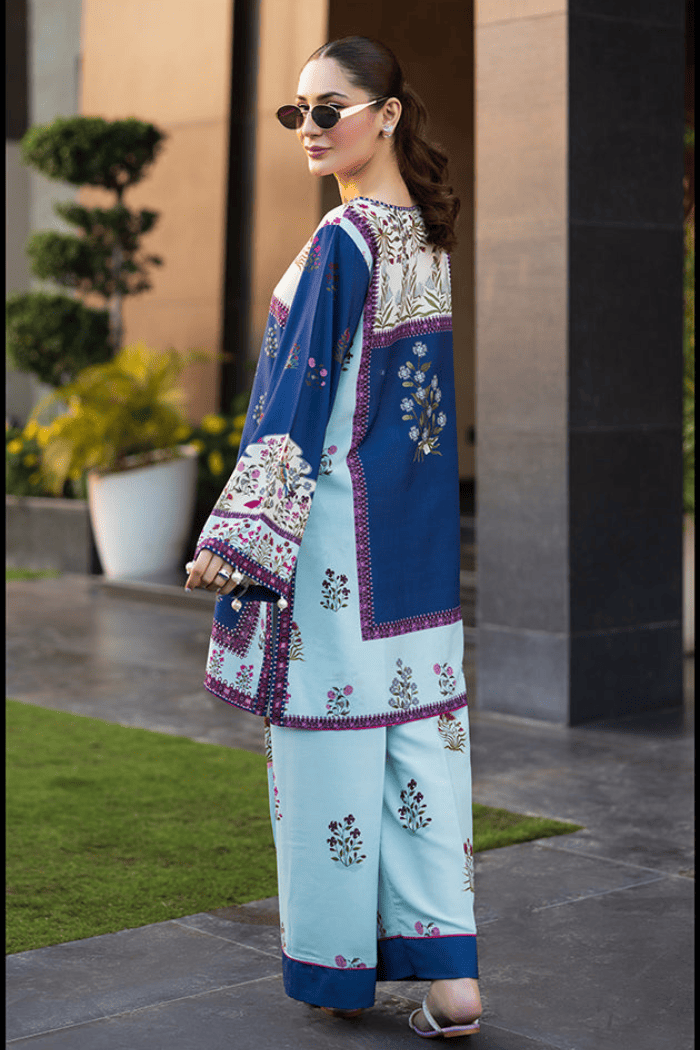 Woman wearing a traditional outfit with a blue and white patterned top and light blue pants, standing outdoors.