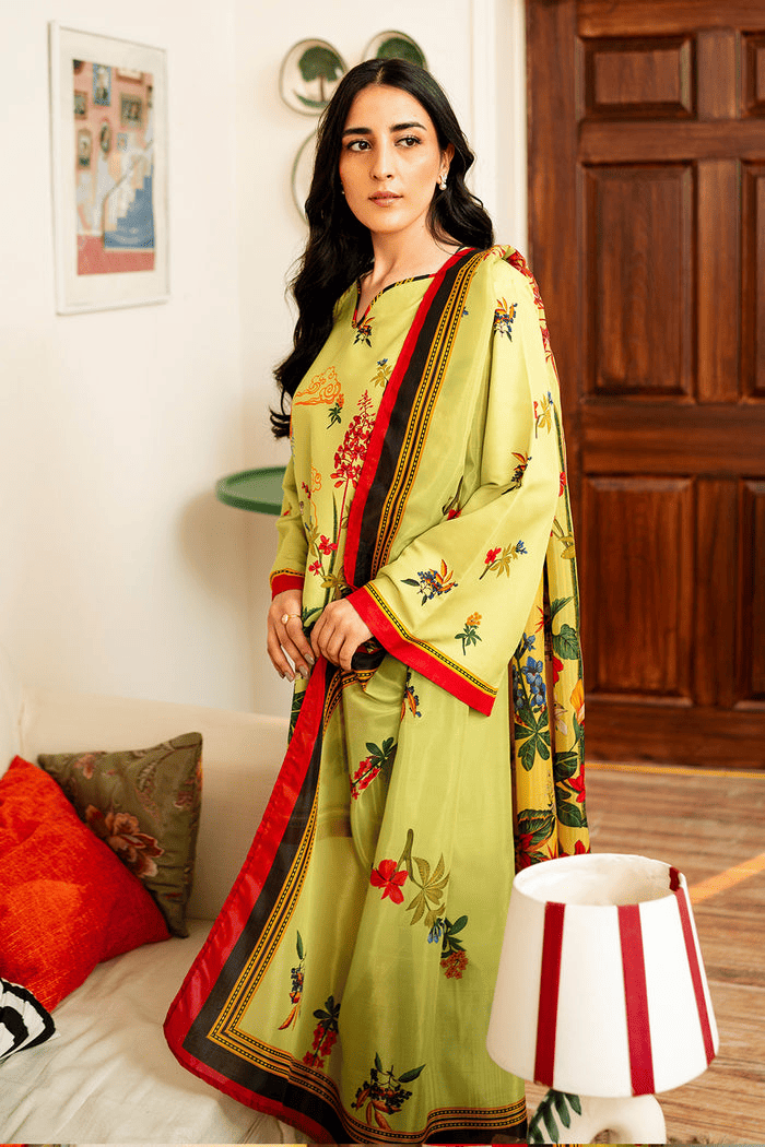 Woman in a green floral saree with red border standing indoors.