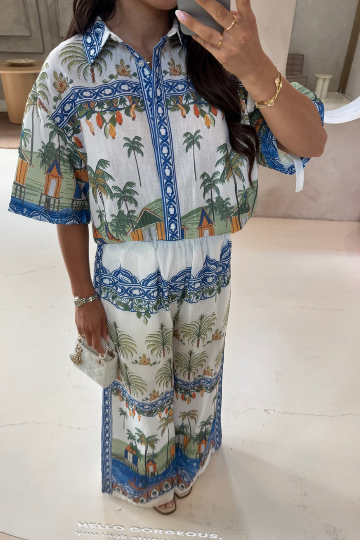 Person wearing a colorful patterned outfit with palm trees and buildings.