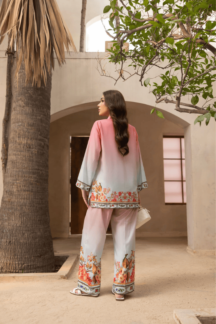 Woman in a floral outfit standing in a sunlit outdoor setting with palm trees and a building.