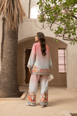 Woman in a floral outfit standing in a sunlit outdoor setting with palm trees and a building.