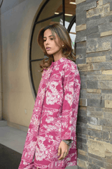 Woman in a pink floral dress standing against a stone wall.