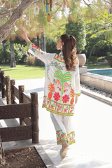 Woman in a colorful traditional outfit standing outdoors with trees and a pool in the background