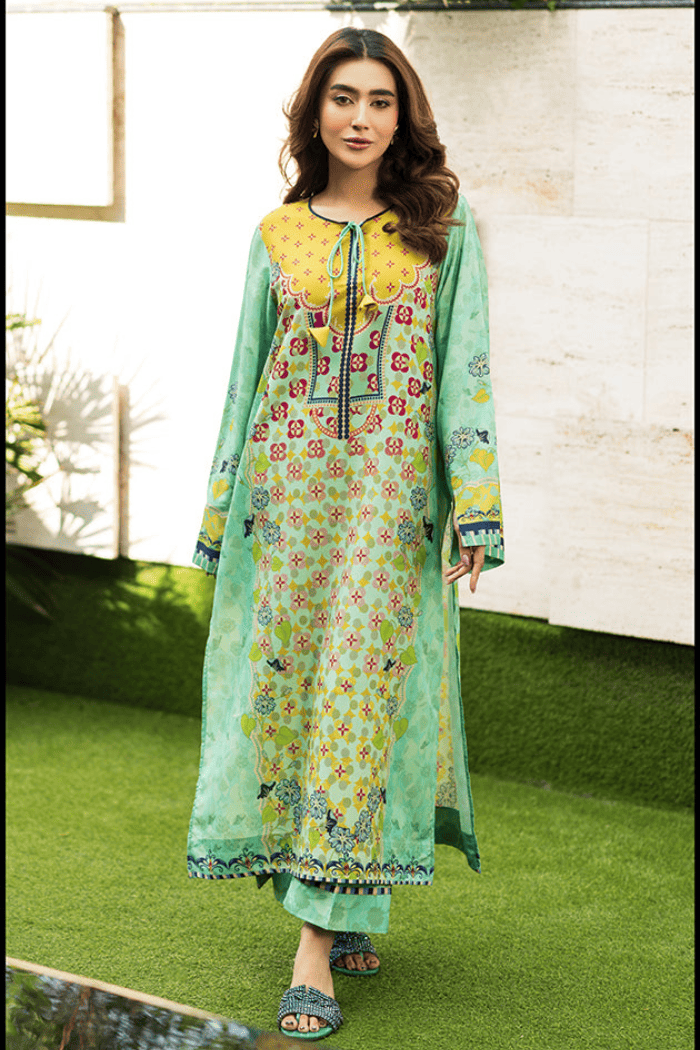 Woman wearing a green floral dress with a yellow top on a grassy area.
