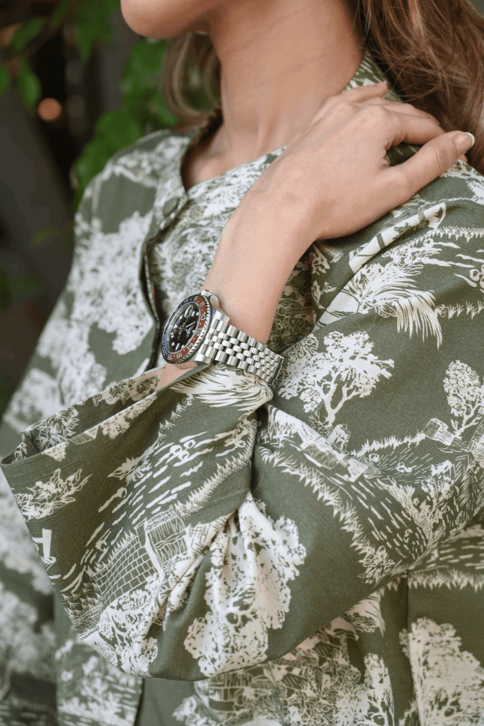 Person wearing a green patterned shirt with a close-up of a wrist wearing a silver watch.