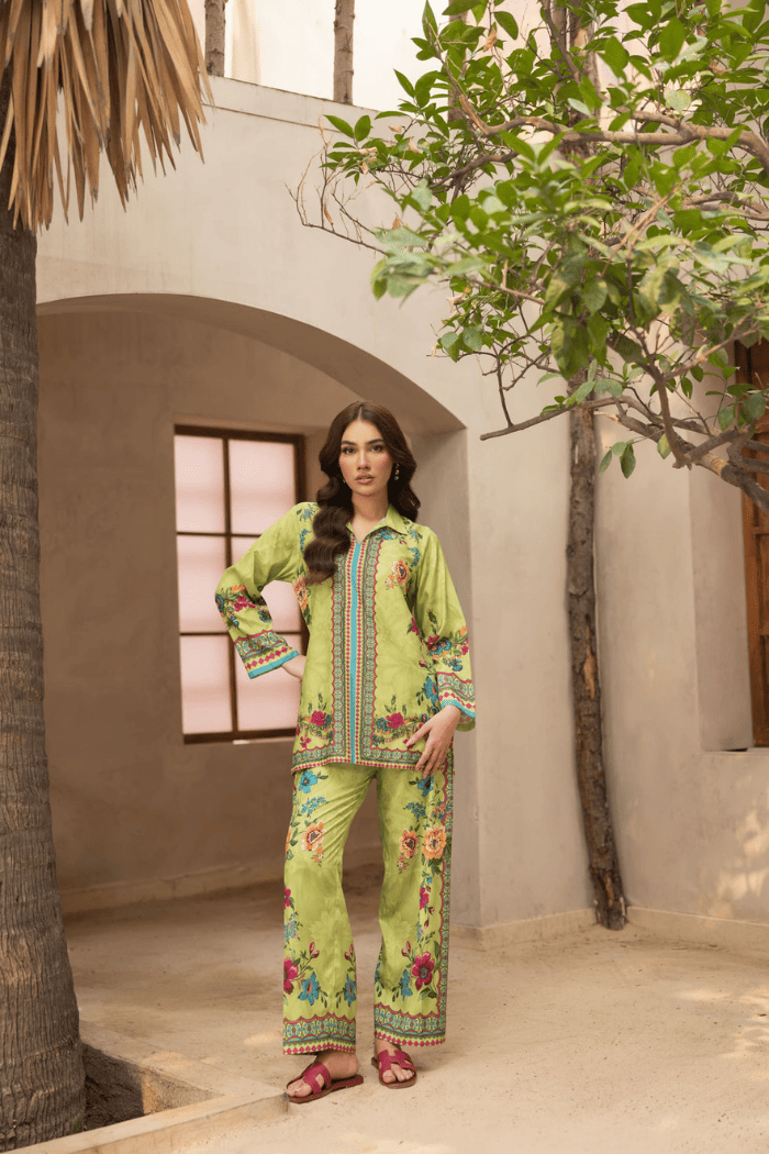 Woman in a green floral outfit standing in a sunlit outdoor setting with architectural elements.
