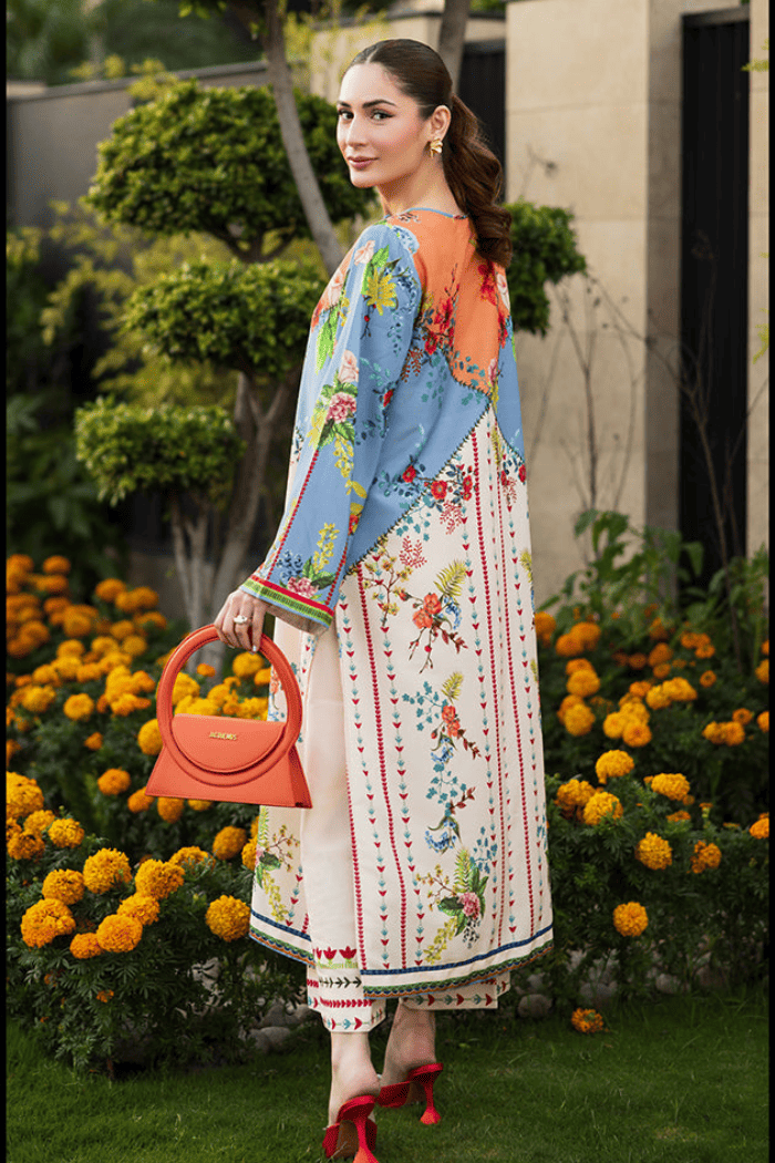Woman in a floral dress with a colorful shawl standing in front of flowers and a building.