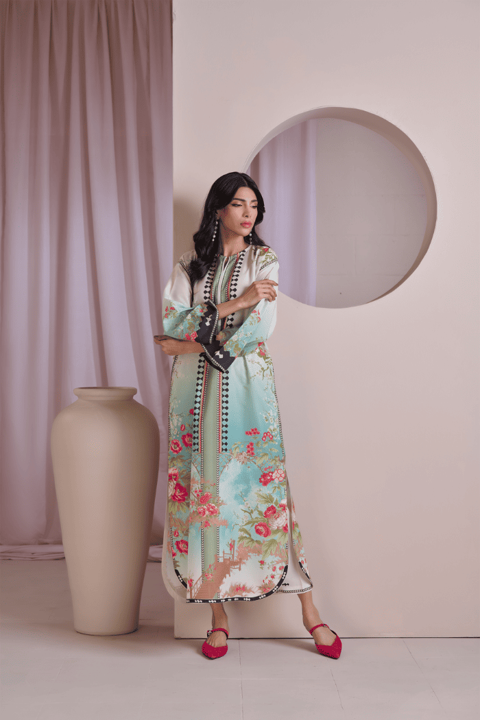 Woman in a floral dress standing next to a large vase against a plain wall.