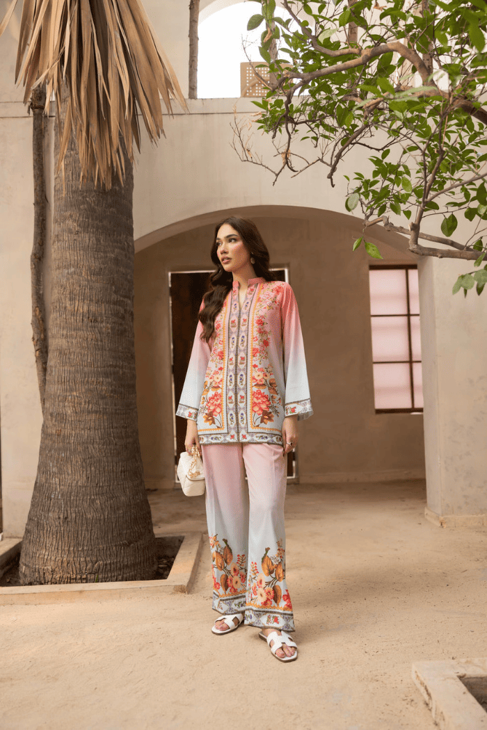Woman in a floral outfit standing in a sunlit courtyard with trees and architectural elements.