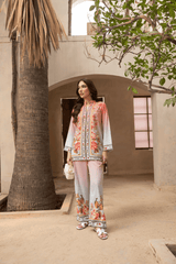 Woman in a floral outfit standing in a sunlit courtyard with trees and architectural elements.