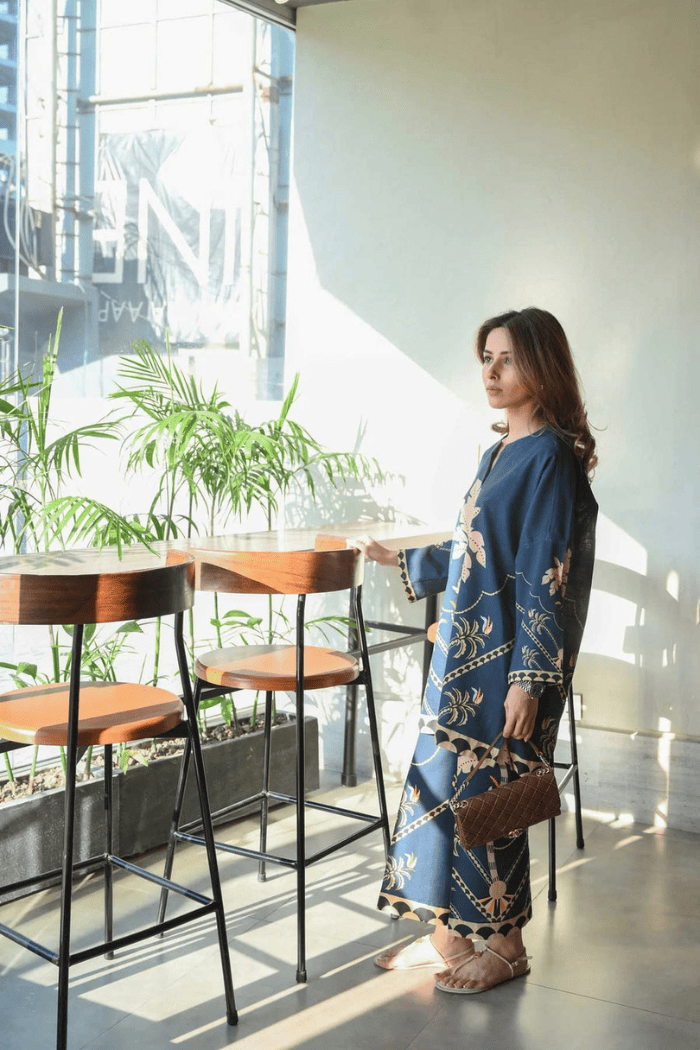 Woman in a blue dress sitting at a high table in a modern cafe.