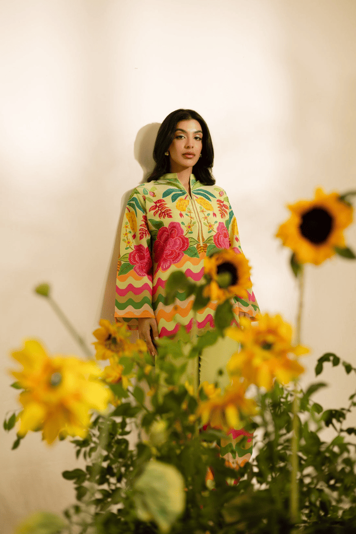 Woman wearing a colorful patterned dress standing among sunflowers.