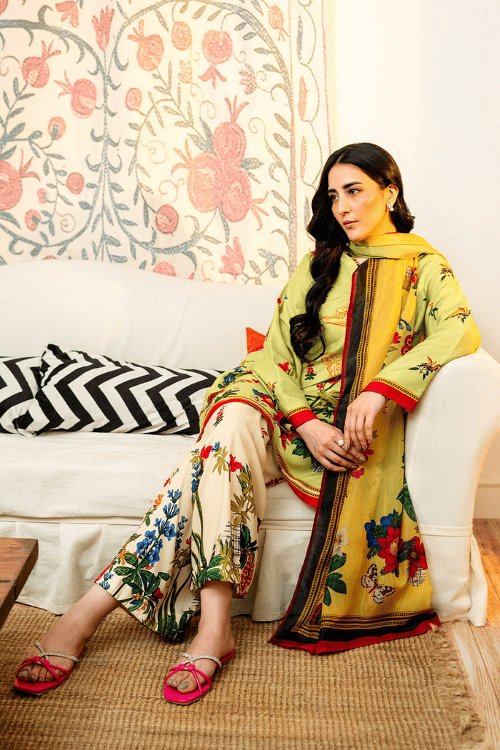 Woman in a yellow embroidered outfit sitting on a couch with floral patterned wall and cushions.