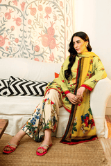 Woman in a yellow embroidered outfit sitting on a couch with floral patterned wall and cushions.