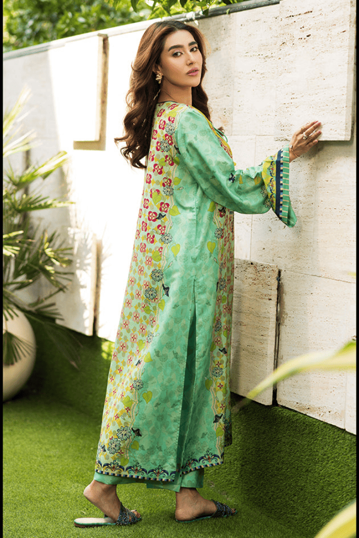 Woman in a floral dress standing against a white wall with green grass below.