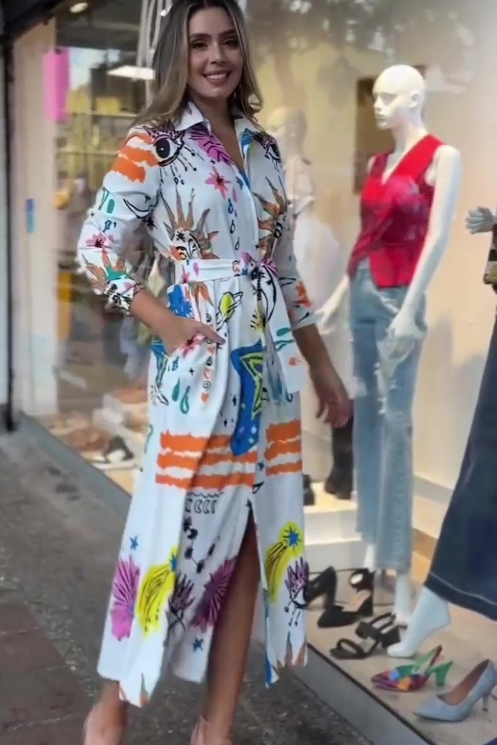 Woman wearing a colorful dress standing in front of a store window with mannequins.