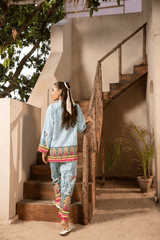 Woman in traditional outfit standing on a staircase with plants and a building in the background