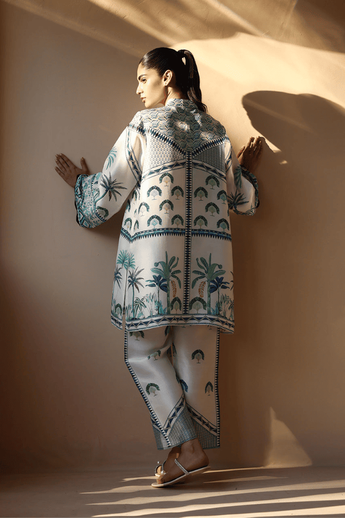 Woman wearing a patterned outfit standing against a plain wall.