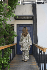 Person in a floral outfit walking towards a blue door with greenery on either side.