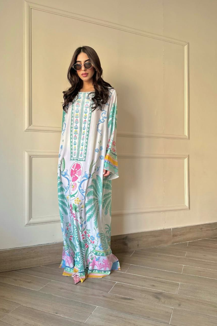 Woman wearing a colorful embroidered dress standing against a neutral wall.