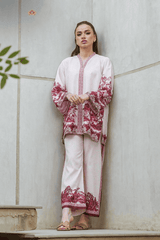 Woman wearing a white outfit with red floral patterns against a light-colored wall.