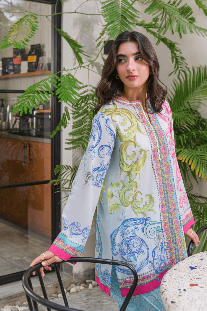 Woman wearing a colorful embroidered dress standing in front of green plants.
